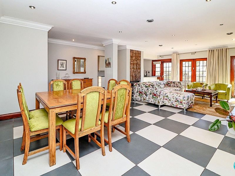 Spacious open-plan living and dining area featuring checkerboard tiled flooring, a stone-clad fireplace, and multiple sets of timber-framed french doors leading outdoors.