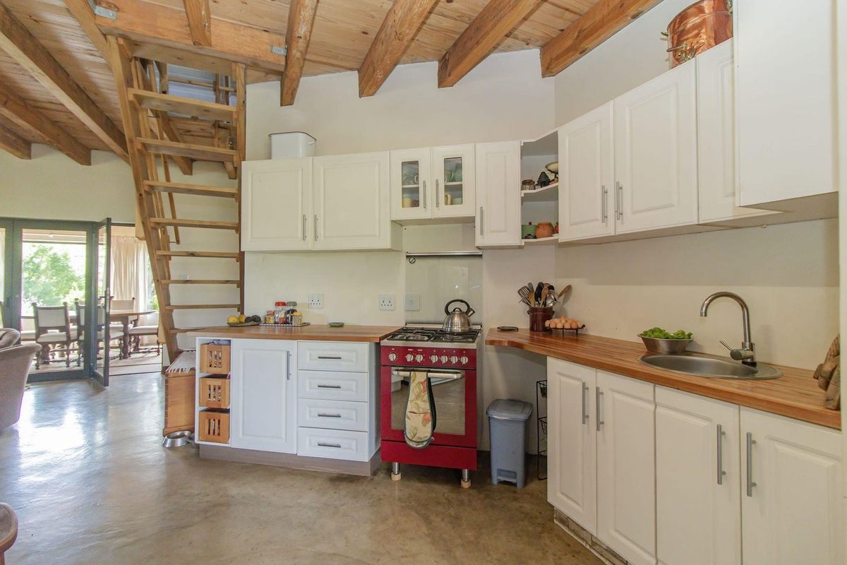 A rustic kitchen featuring white cabinetry, wooden countertops, a red gas stove, and an exposed timber beam ceiling with an integrated staircase.