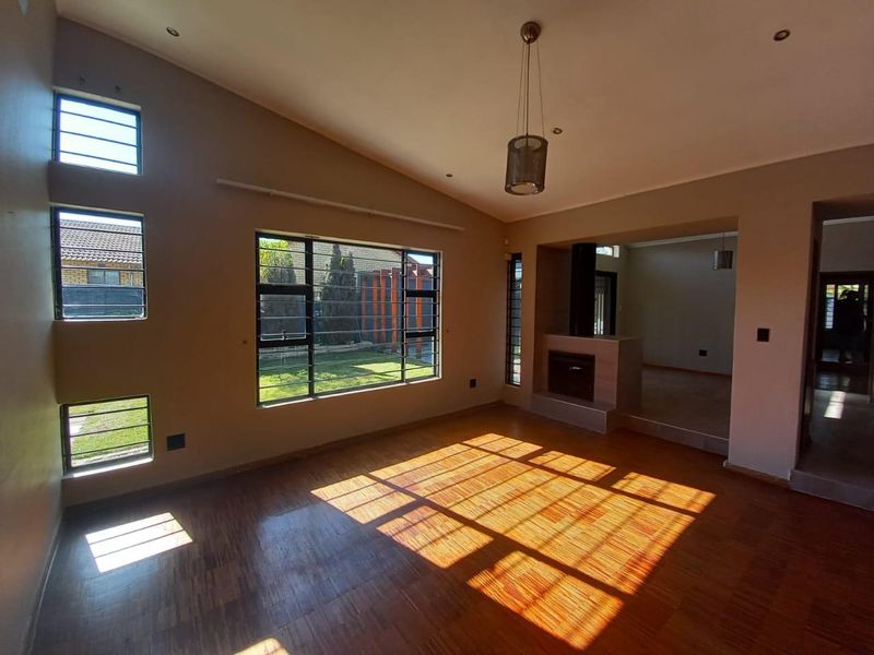 Spacious living room featuring warm parquet flooring, a built-in fireplace, vaulted ceilings, and large windows that provide ample natural light.
