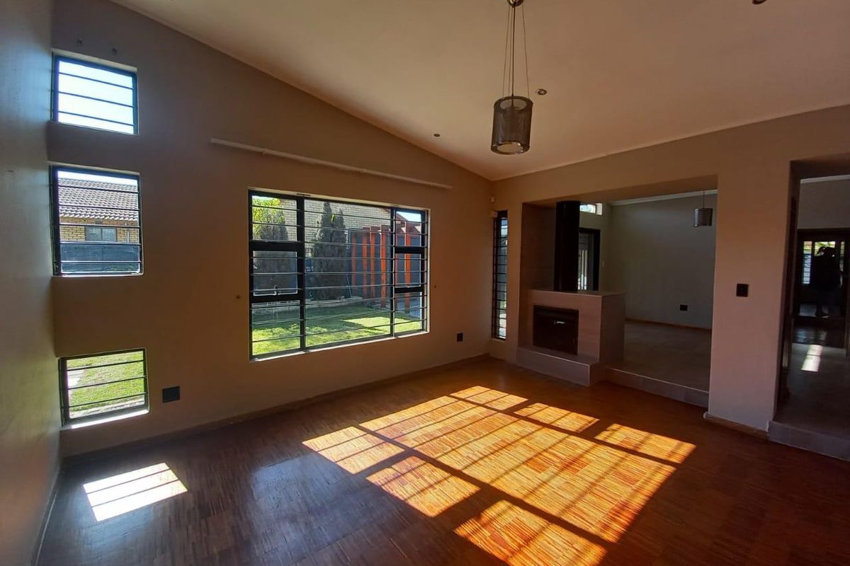 Spacious living room featuring warm parquet flooring, a built-in fireplace, vaulted ceilings, and large windows that provide ample natural light.