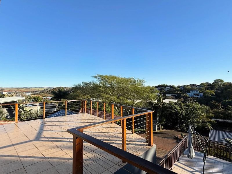 Spacious elevated balcony featuring tiled flooring and a timber handrail with cable balustrade, offering expansive views of the surrounding neighborhood.