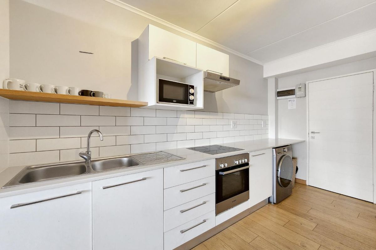 Modern kitchen featuring white cabinetry, subway tile backsplash, integrated appliances including an oven and cooktop, and durable laminate flooring.
