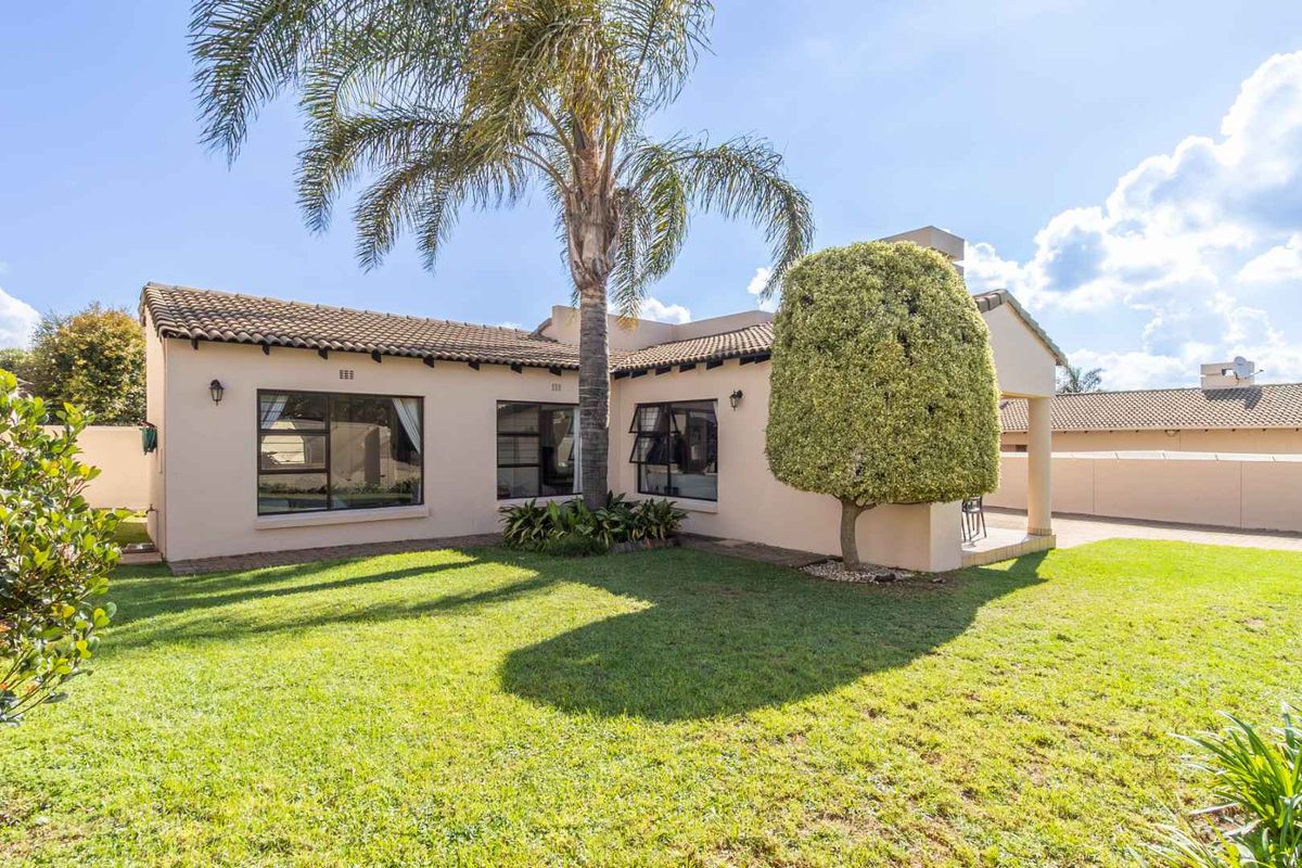 A well-maintained rear exterior view of the cluster home featuring a landscaped garden, paved patio area, and established trees.