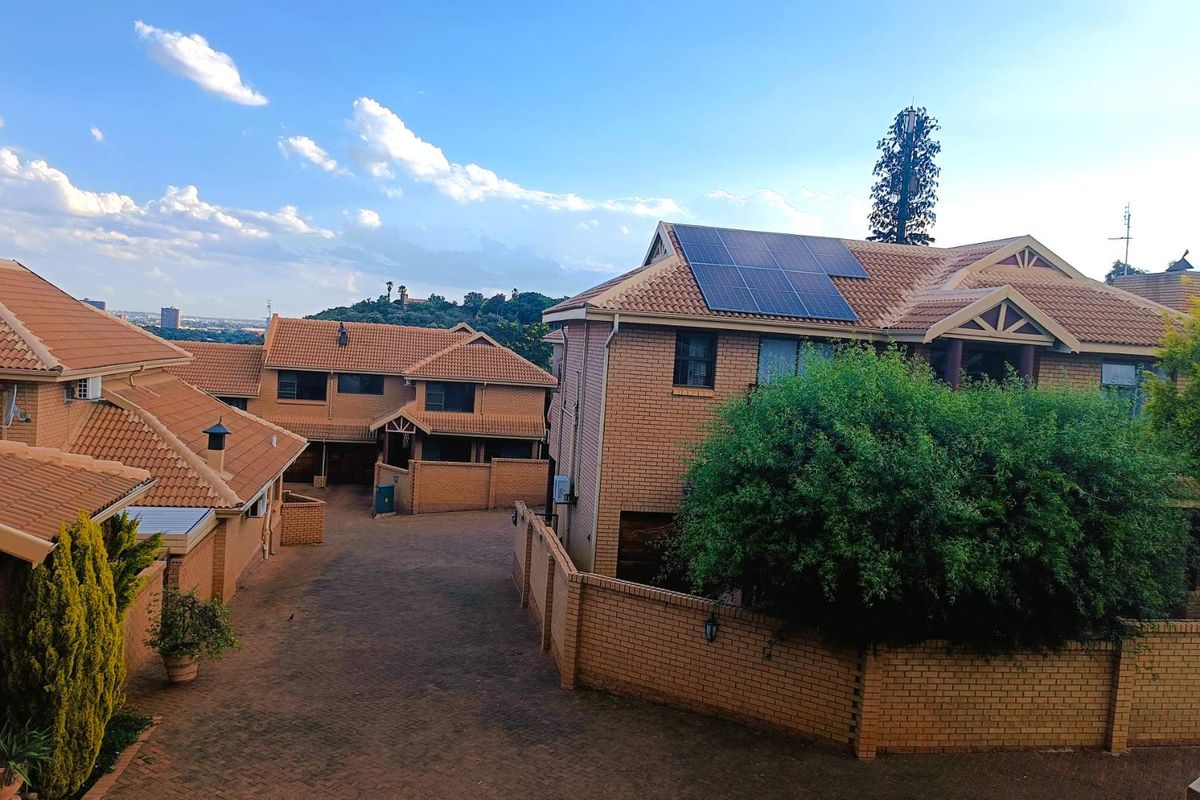 Elevated view of a townhouse complex featuring face-brick facades, tiled roofs, and solar panel installations on the roof.