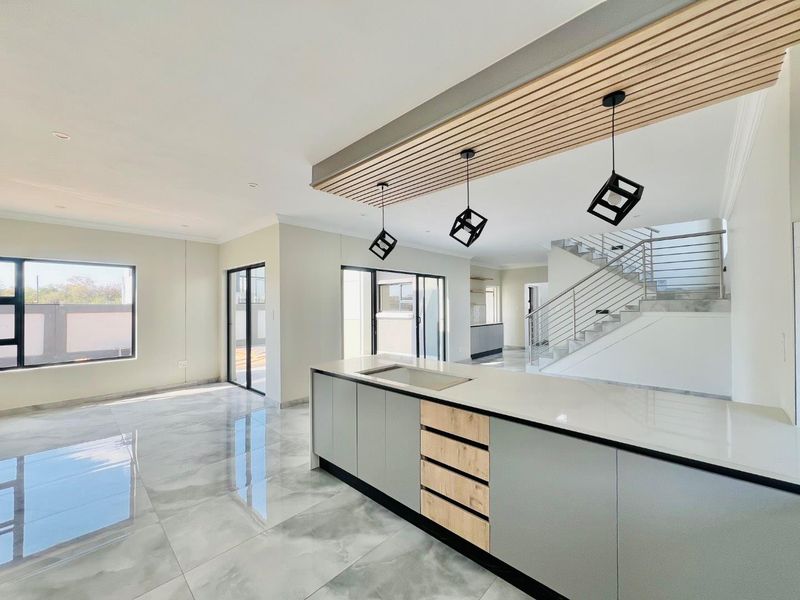 Modern open-plan living area featuring a sleek kitchen island with stone countertops, slatted timber ceiling detail, and a contemporary staircase with stainless steel balustrades.