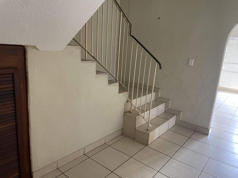 A functional hallway area featuring a tiled staircase with a metal balustrade and a built-in storage cupboard.