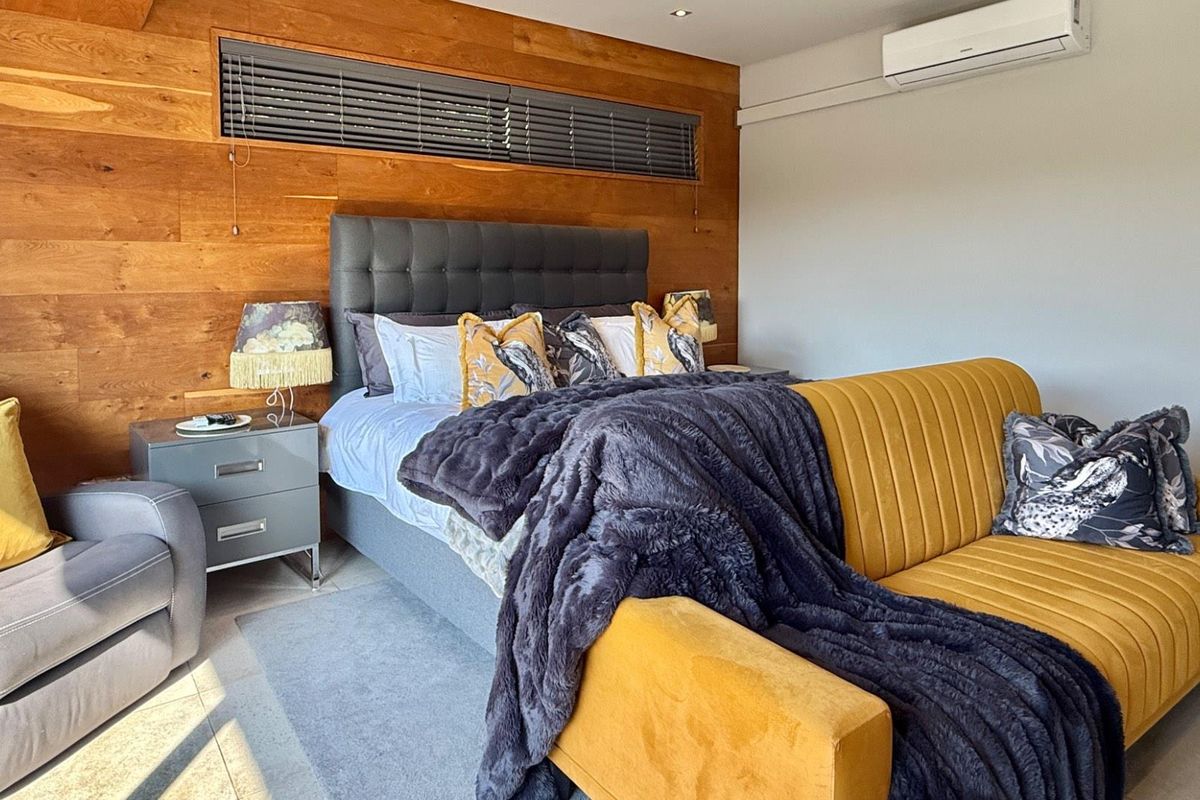 A well-appointed bedroom featuring warm timber wall paneling, tiled flooring, and a wall-mounted air conditioning unit.