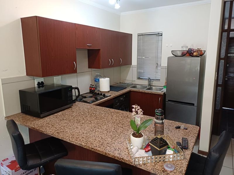 A functional kitchen featuring dark wood-look cabinetry, granite countertops, a breakfast bar, and a double basin sink with a tiled backsplash.