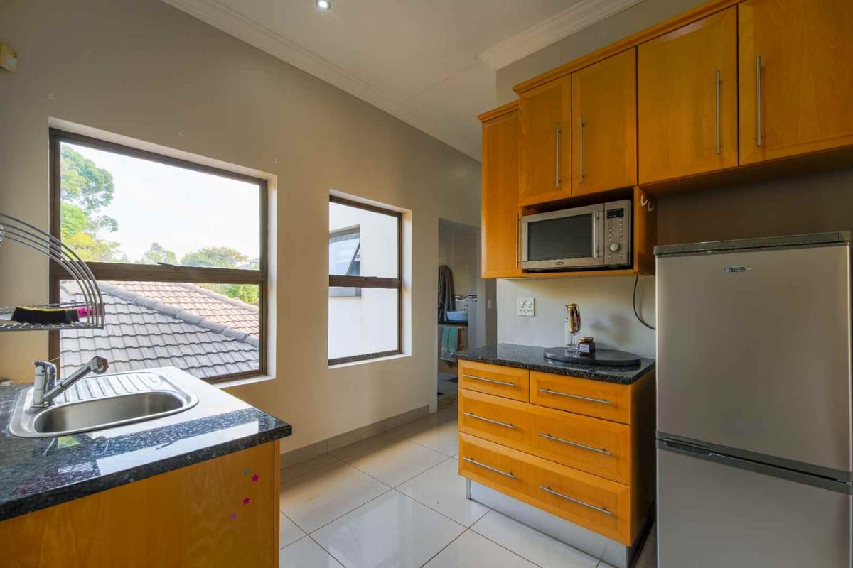 A functional kitchen featuring wooden cabinetry, granite countertops, a stainless steel sink, and tiled flooring with natural light from large windows.