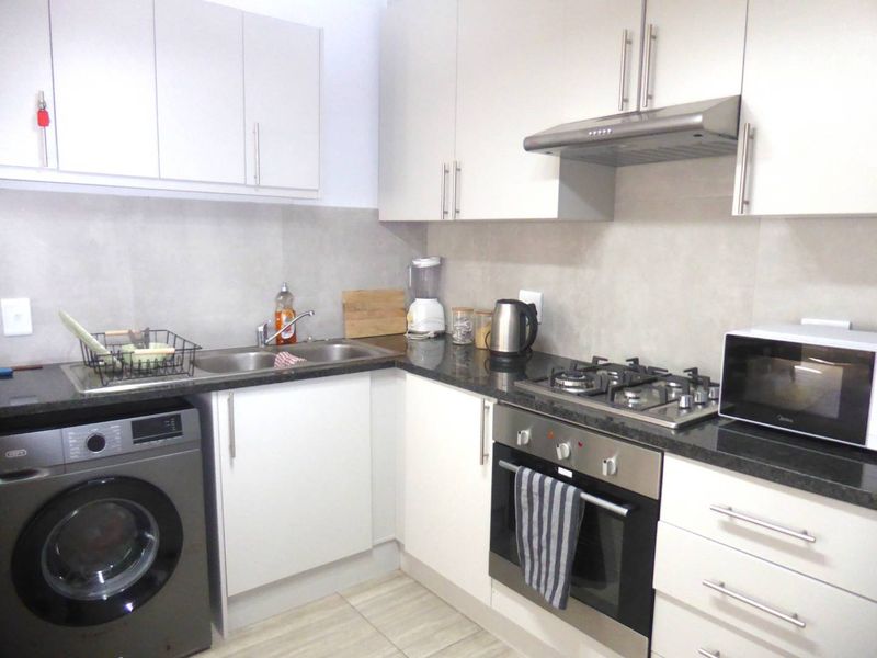 Modern kitchen featuring white cabinetry, granite countertops, stainless steel appliances including a gas hob, oven, and extractor fan, with neutral tiled finishes.
