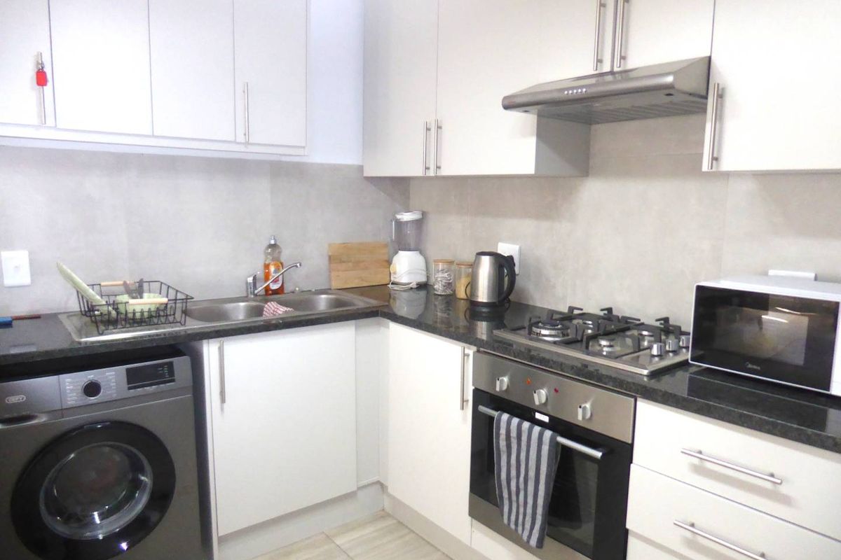 Modern kitchen featuring white cabinetry, granite countertops, stainless steel appliances including a gas hob, oven, and extractor fan, with neutral tiled finishes.
