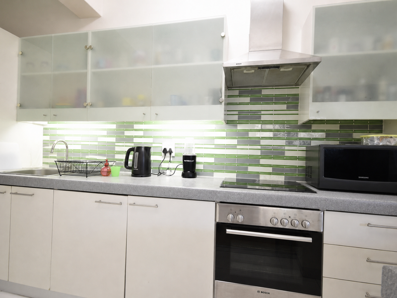 Modern kitchen featuring frosted glass cabinetry, stainless steel appliances including a built-in oven and extractor fan, and a decorative tiled backsplash.