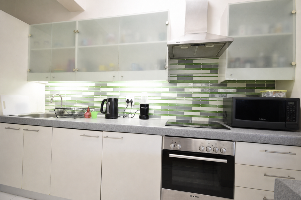 Modern kitchen featuring frosted glass cabinetry, stainless steel appliances including a built-in oven and extractor fan, and a decorative tiled backsplash.
