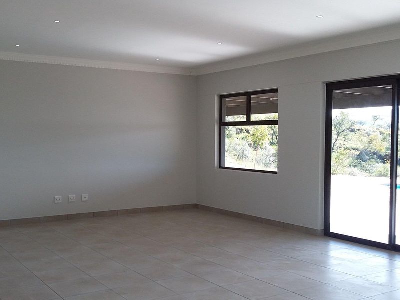 Spacious, light-filled living area featuring neutral tiled flooring, recessed downlighting, and large sliding glass doors providing access to the outdoor pool area.