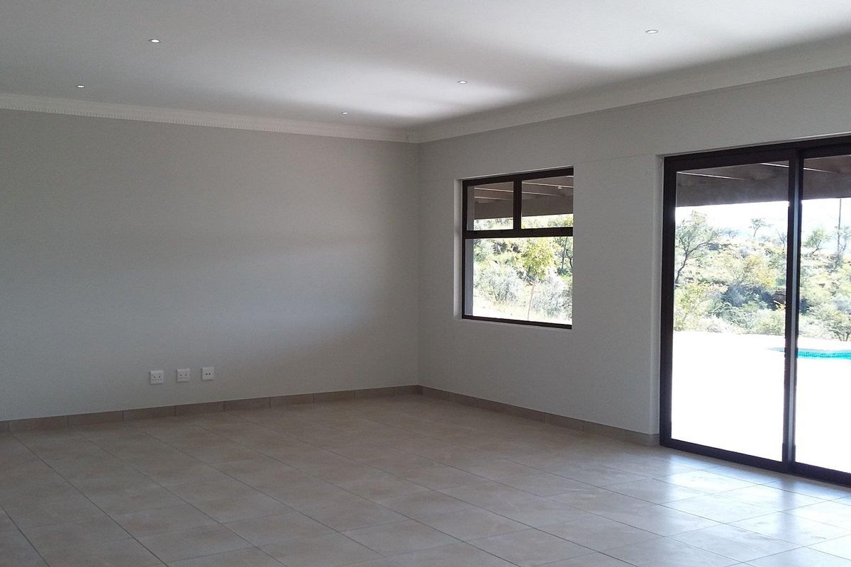 Spacious, light-filled living area featuring neutral tiled flooring, recessed downlighting, and large sliding glass doors providing access to the outdoor pool area.