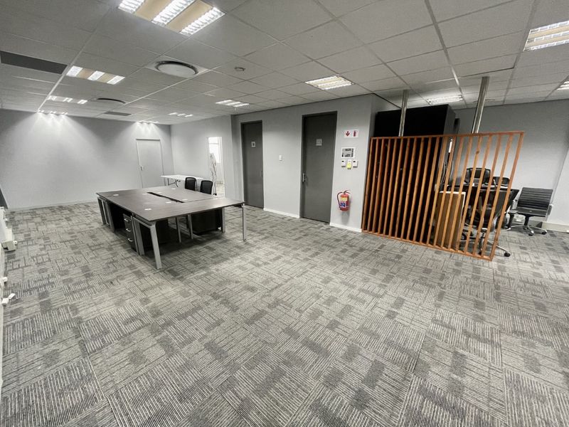 A spacious open-plan office area featuring carpeted flooring, a suspended ceiling with recessed lighting, and a decorative wooden slat partition.