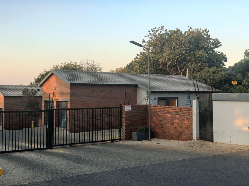 Front entrance view of the apartment complex featuring brick facade buildings, paved driveway, and secure gated access with electric fencing.
