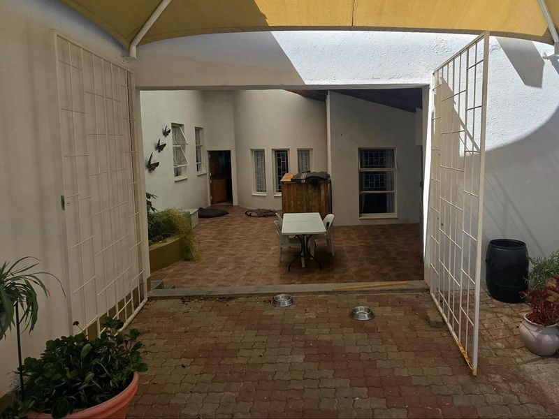 A covered outdoor patio area featuring tiled flooring, security gates, and a shade sail, providing a functional space for outdoor living.