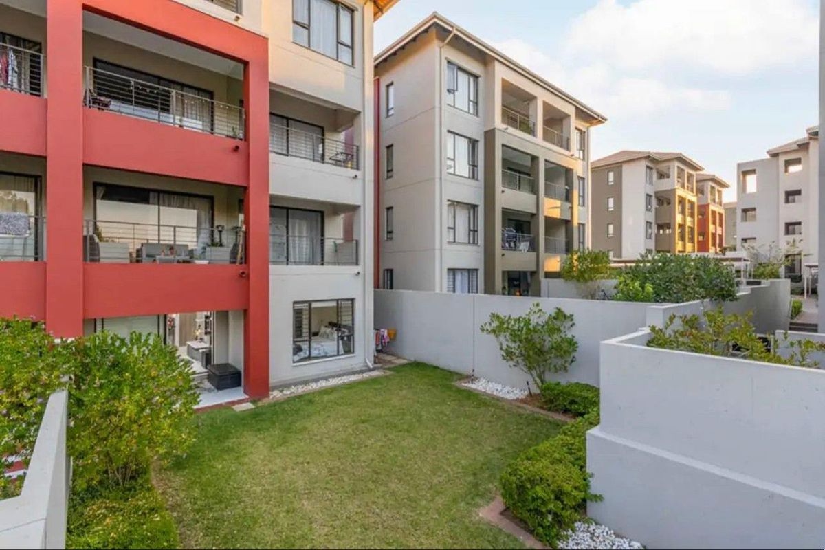 Rear view of a modern apartment complex featuring private balconies, ground floor garden access, and well-maintained exterior finishes.