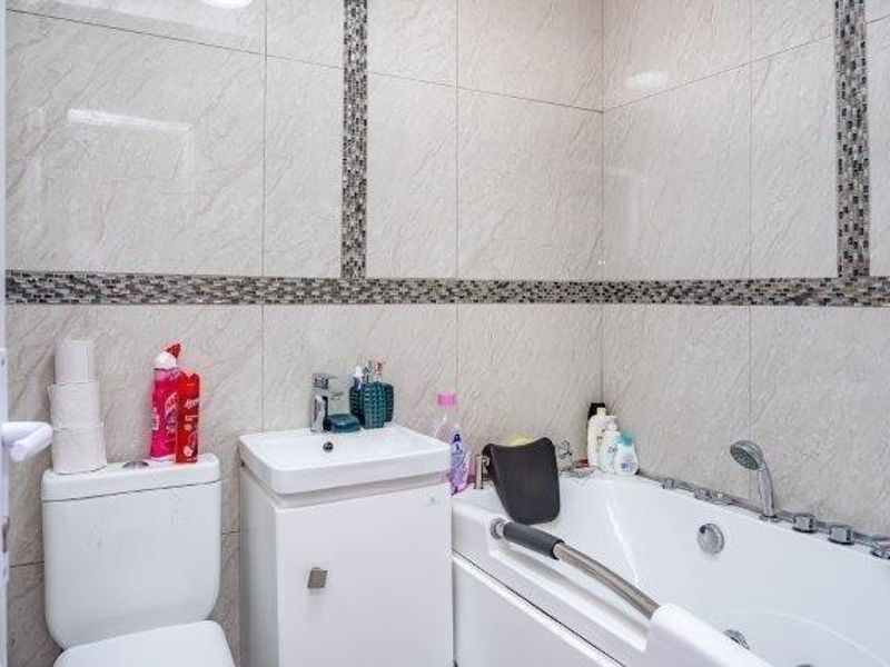 A well-maintained bathroom featuring modern ceramic wall tiles with mosaic accents, a vanity basin, a toilet, and a bathtub with a shower attachment.