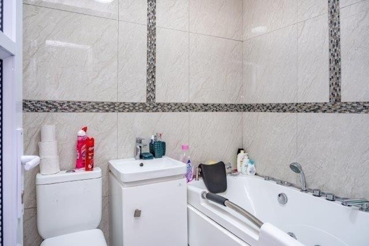 A well-maintained bathroom featuring modern ceramic wall tiles with mosaic accents, a vanity basin, a toilet, and a bathtub with a shower attachment.