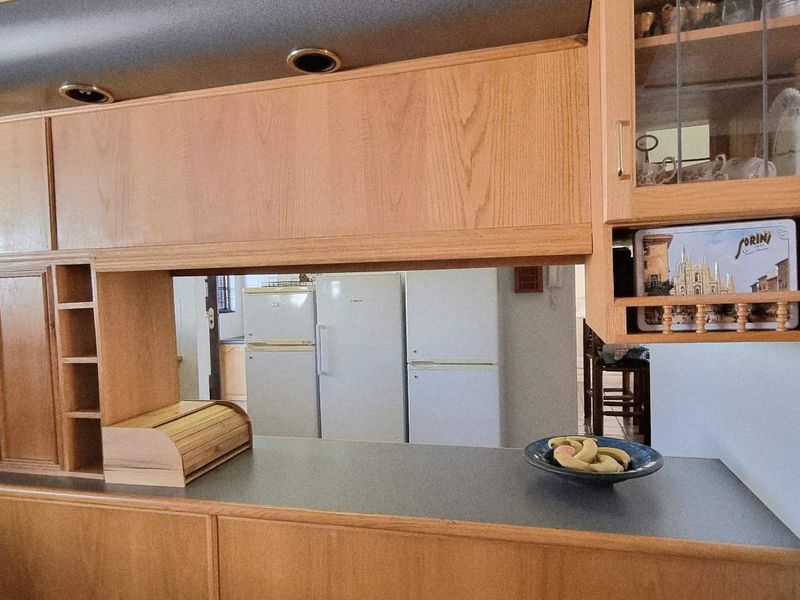 A kitchen featuring traditional timber cabinetry, laminate countertops, and recessed lighting, offering a functional layout with a pass-through window to the adjacent area.