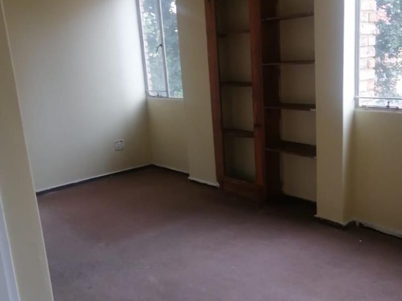 An empty bedroom featuring built-in wooden shelving, carpeted flooring, and large windows providing natural light.