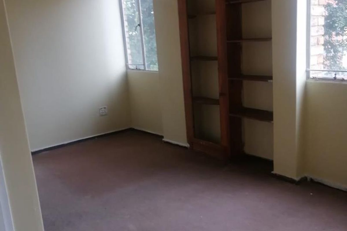 An empty bedroom featuring built-in wooden shelving, carpeted flooring, and large windows providing natural light.