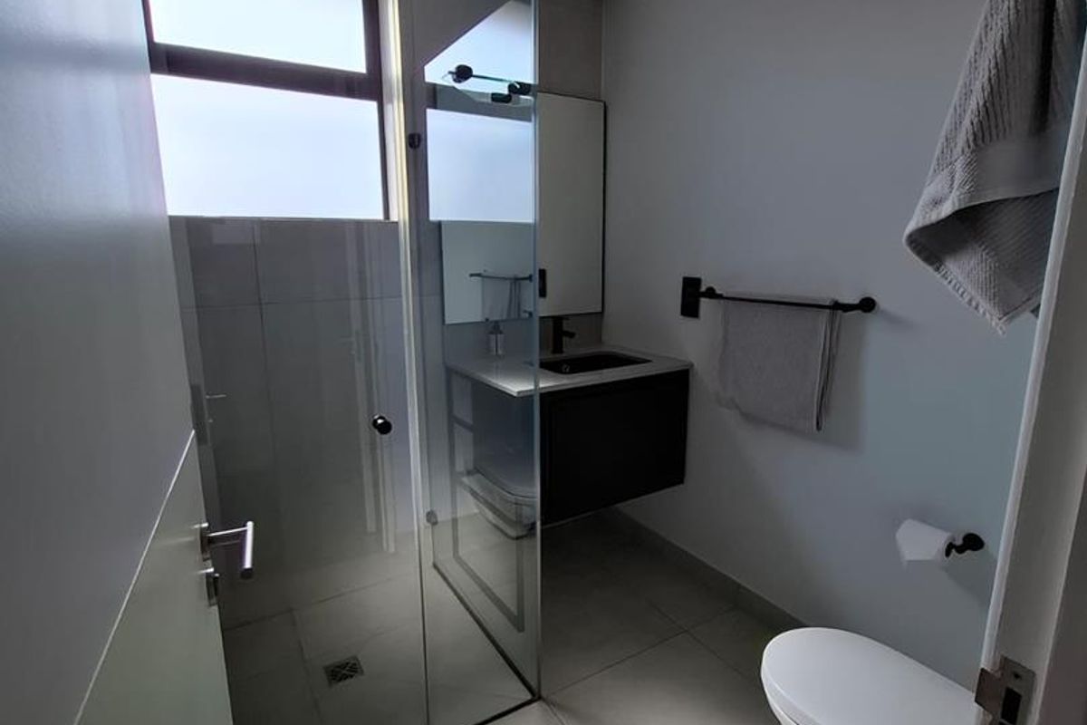 Modern bathroom featuring a glass-enclosed shower, wall-mounted vanity, and contemporary fixtures with neutral floor tiling.