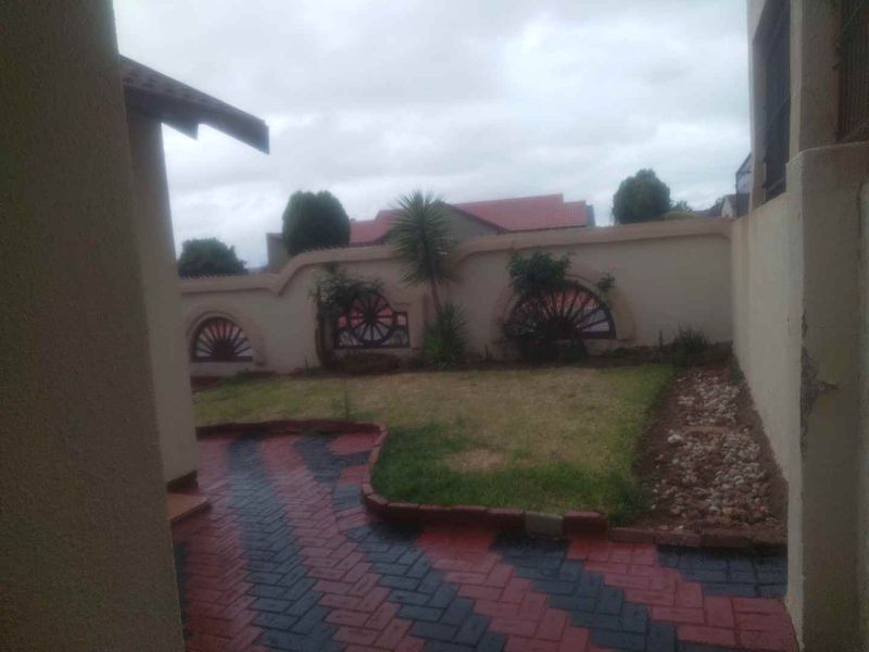 A rear garden area featuring a paved patio, a small lawn, and a decorative boundary wall.