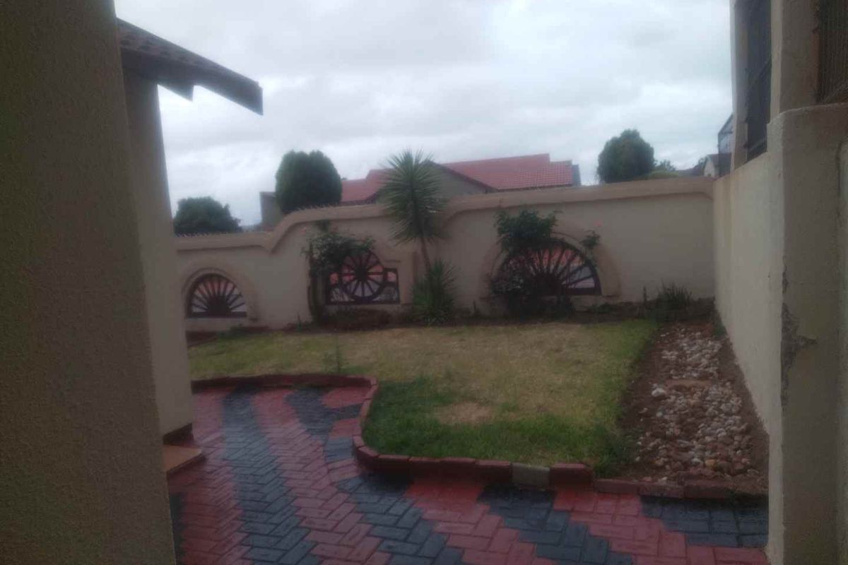 A rear garden area featuring a paved patio, a small lawn, and a decorative boundary wall.