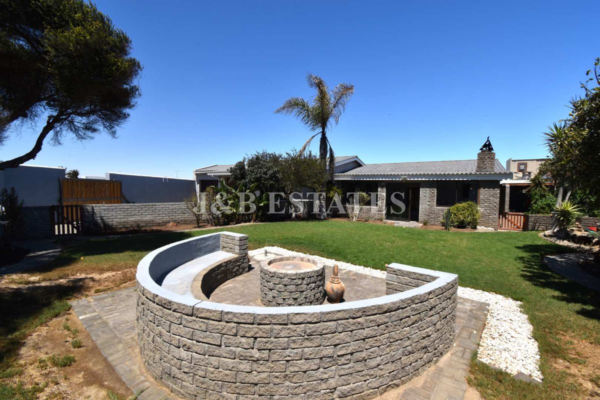 A spacious rear garden featuring a built-in circular stone fire pit with integrated seating, set against the rear elevation of the house.