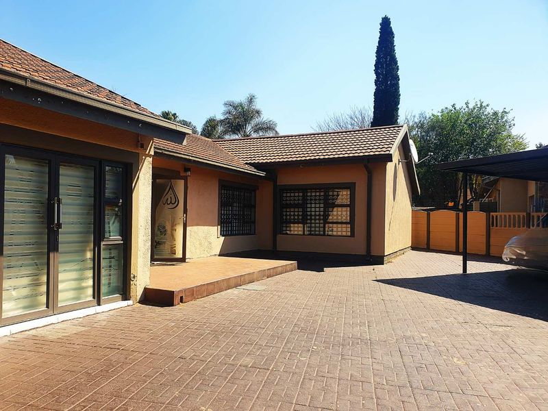 Rear exterior view featuring a paved driveway, tiled patio area, carport, and secure window bars on a well-maintained residential property.