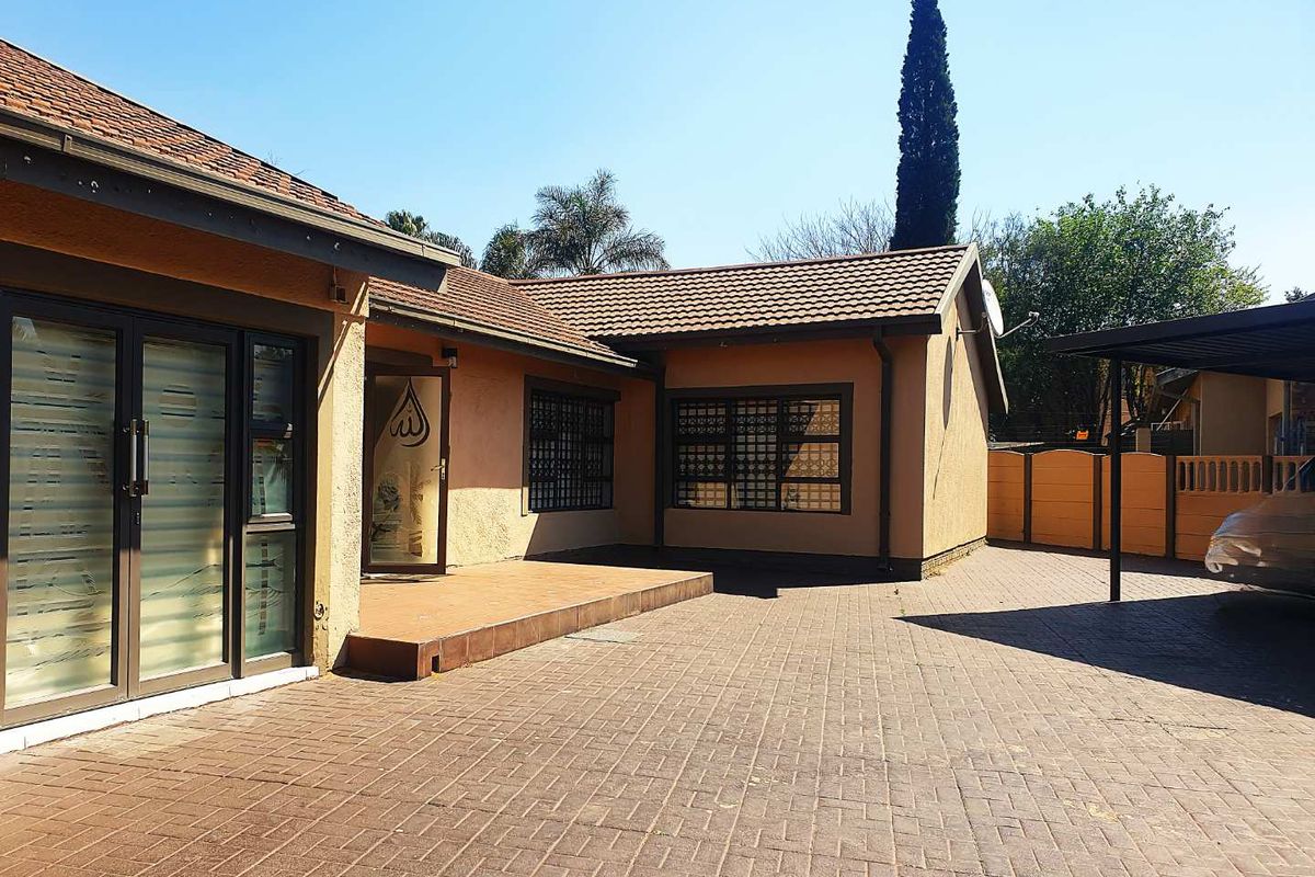 Rear exterior view featuring a paved driveway, tiled patio area, carport, and secure window bars on a well-maintained residential property.
