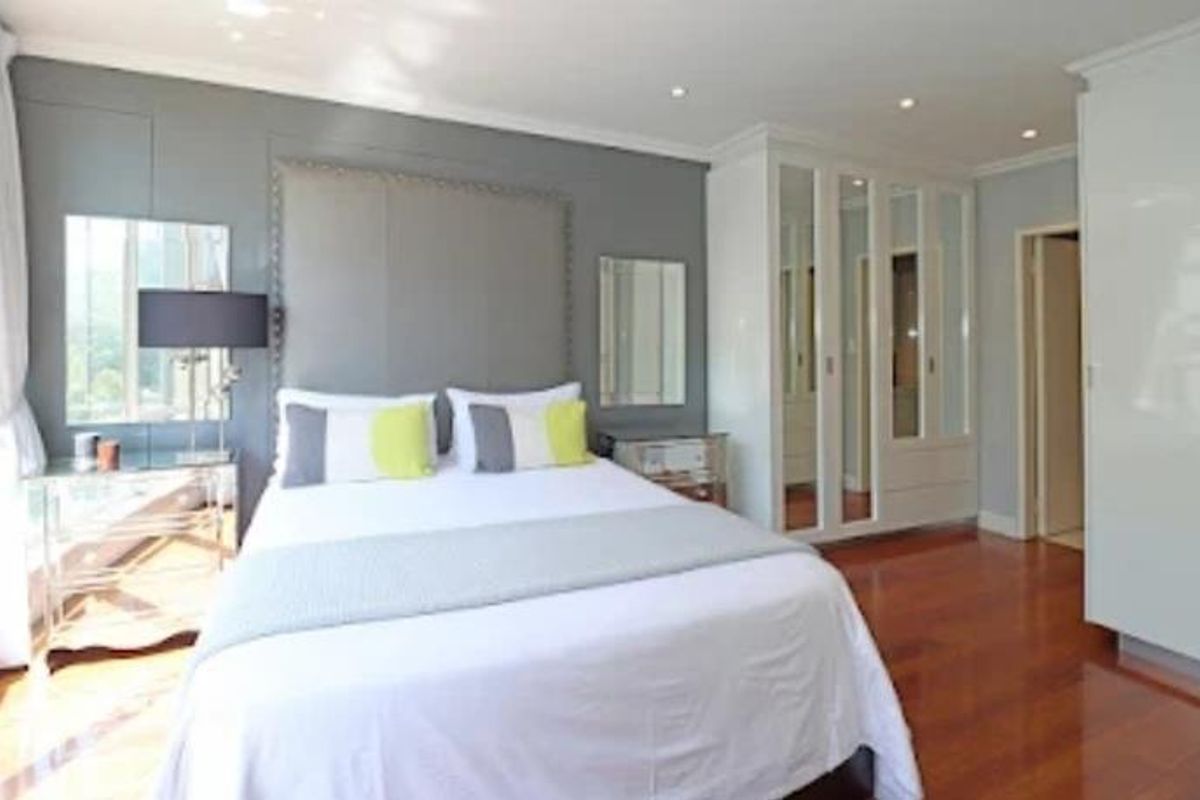 A well-maintained bedroom featuring polished hardwood flooring, extensive built-in mirrored wardrobes, and recessed ceiling lighting.