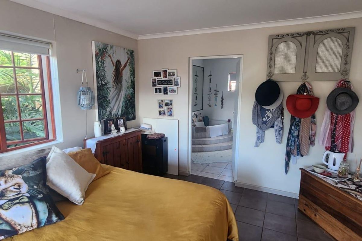 A bedroom featuring tiled flooring, a large window with garden views, and an adjoining en-suite bathroom area.