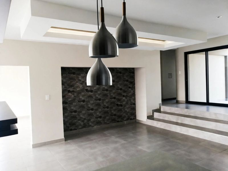 Modern living area featuring a recessed ceiling, stone accent wall, tiled flooring, and a stepped transition leading to a sliding glass door.