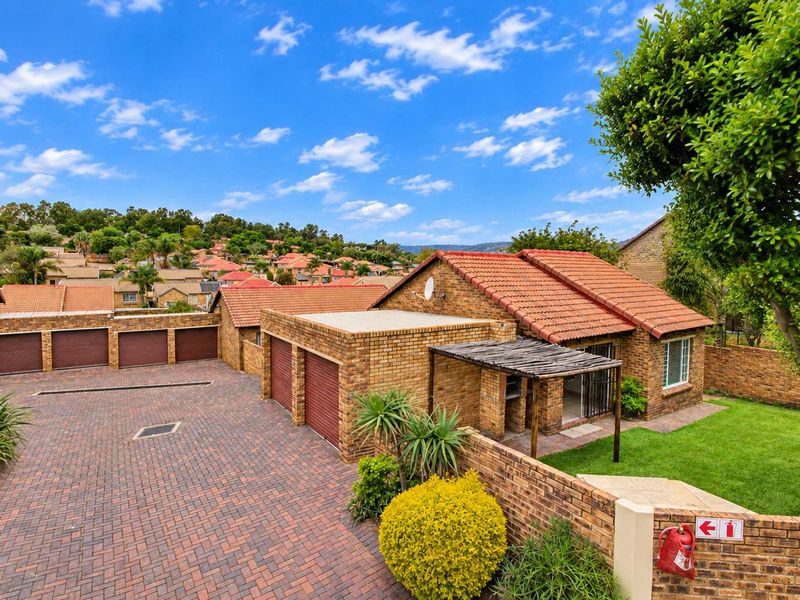A well-maintained face brick townhouse featuring a paved driveway, double garage, and a covered patio area with a built-in braai.