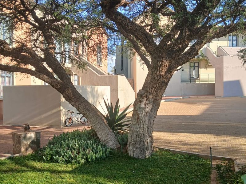 A view of the apartment complex rear courtyard featuring a paved area, landscaped garden, and external building access stairs.