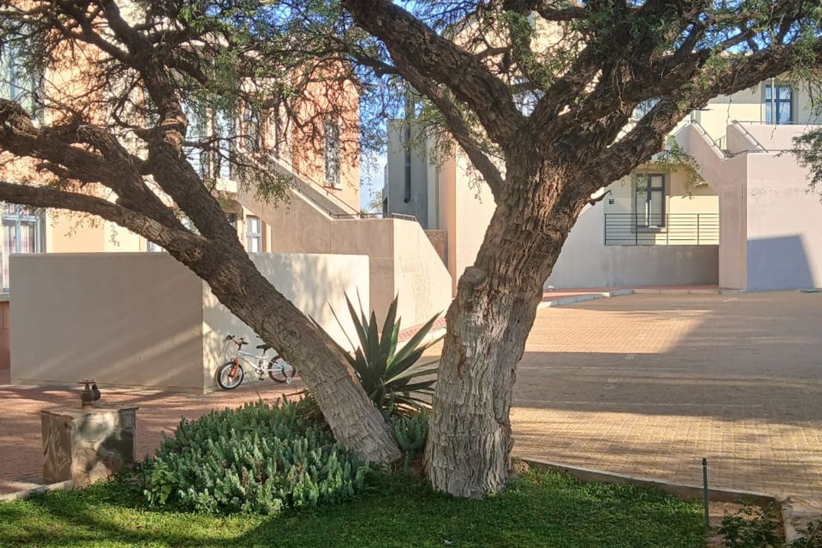 A view of the apartment complex rear courtyard featuring a paved area, landscaped garden, and external building access stairs.
