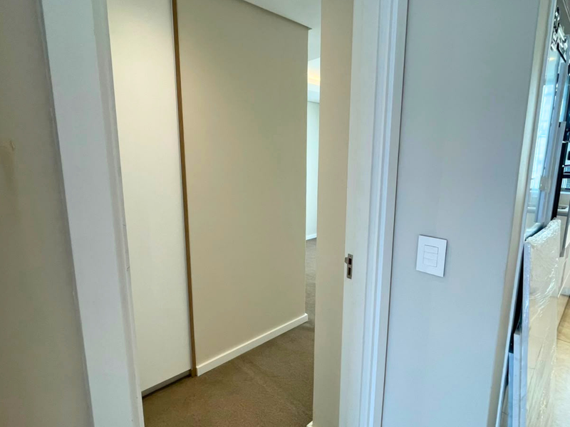 A clean, neutral-toned hallway featuring built-in cupboards and carpeted flooring, providing a seamless transition between living spaces in this modern apartment.