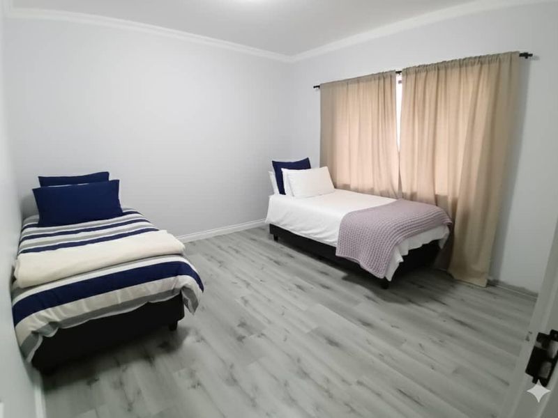 A clean, well-maintained bedroom featuring modern grey laminate flooring, neutral wall finishes, and a window fitted with a curtain rod.