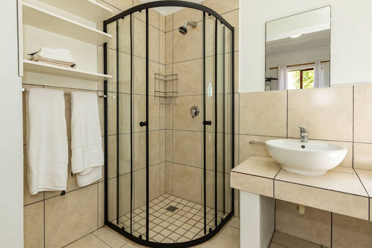 A functional bathroom featuring a corner shower enclosure with black framing, a tiled vanity with a vessel sink, and built-in wall shelving.