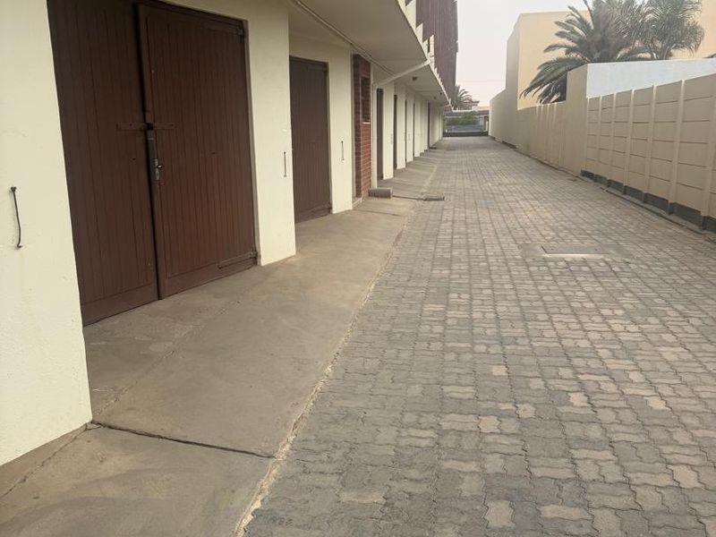 A row of garage units with paved access driveway and perimeter boundary walling.