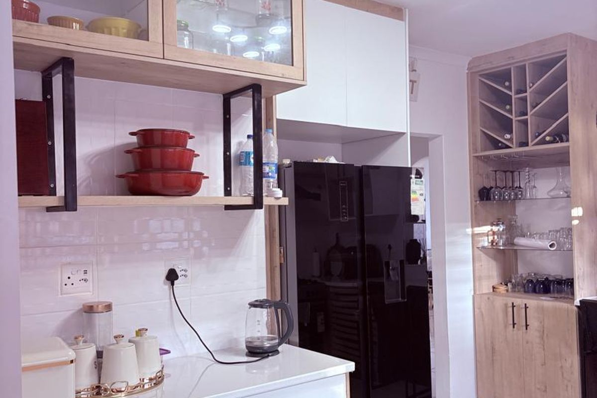 A modern kitchen featuring light wood-toned cabinetry, glass display units, a built-in wine rack, and a clean tiled backsplash with contemporary finishes.