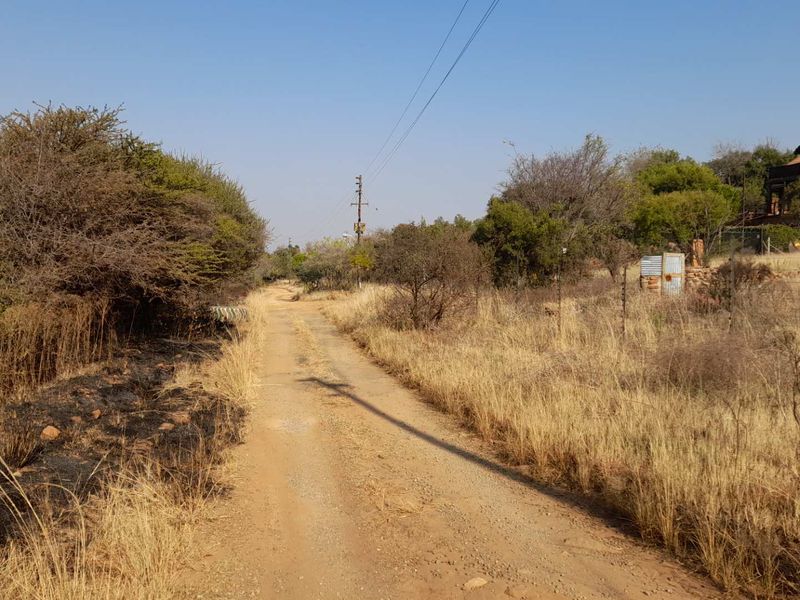 A view of a dirt access road leading towards the property, featuring overhead power lines and surrounding natural vegetation.