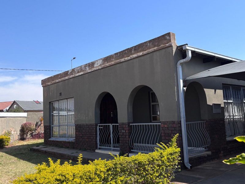 Front elevation of a single-story house featuring an arched porch, brick detailing, and security bars on windows.