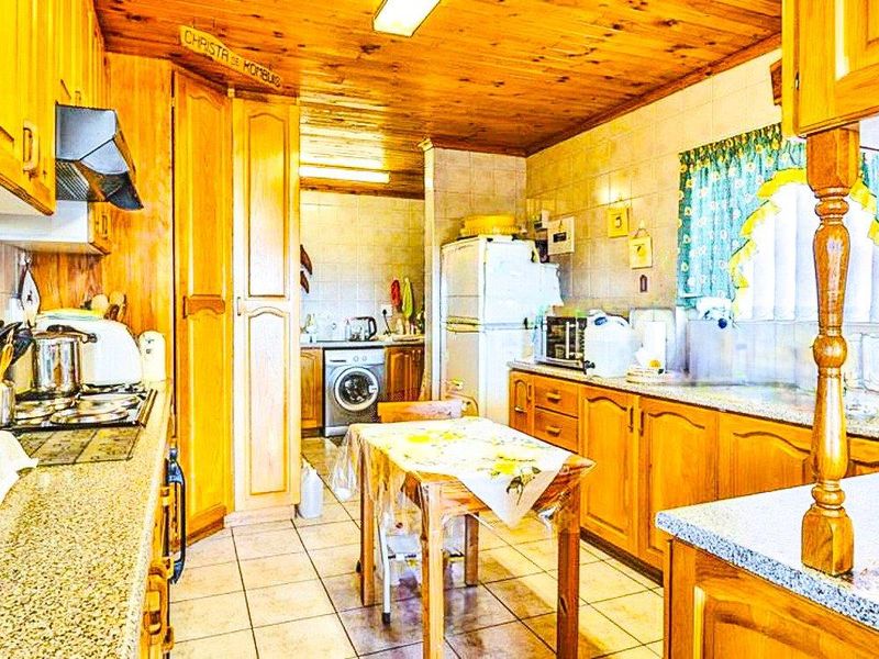 A dated kitchen featuring extensive wooden cabinetry, granite countertops, and a timber ceiling, with an integrated laundry area and tiled finishes throughout.