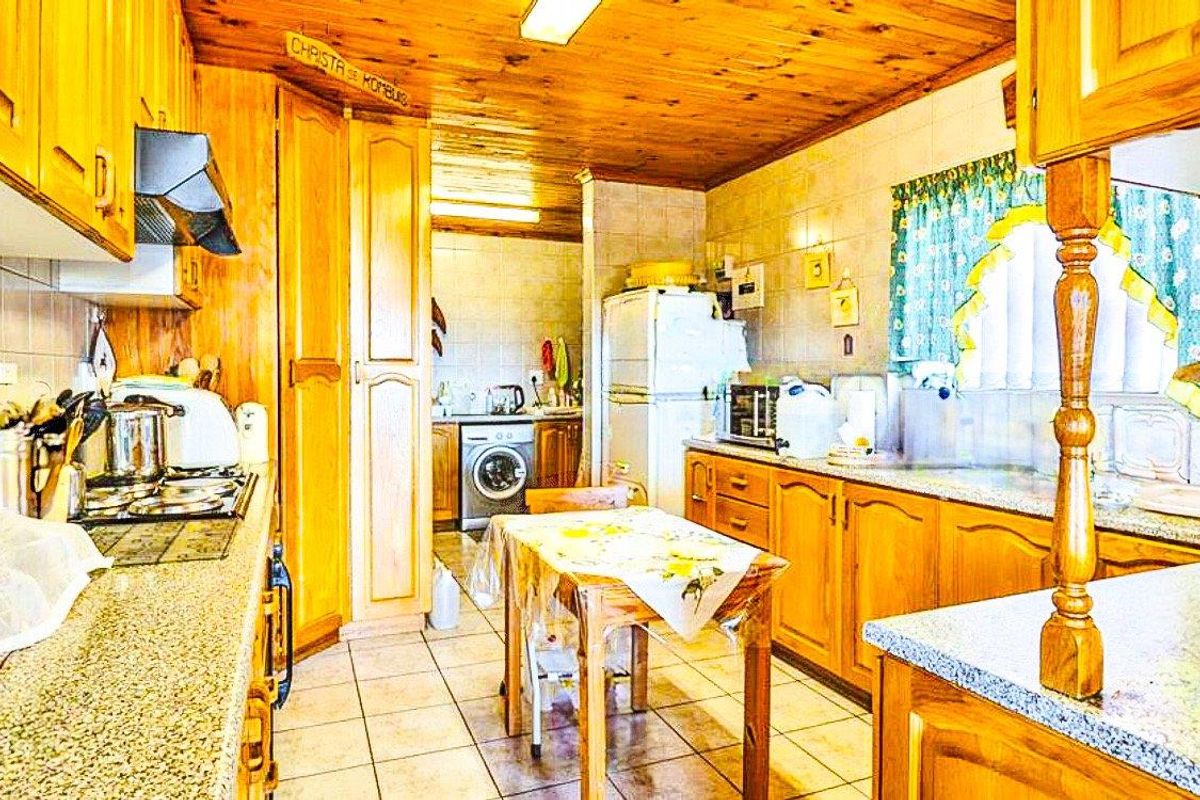 A dated kitchen featuring extensive wooden cabinetry, granite countertops, and a timber ceiling, with an integrated laundry area and tiled finishes throughout.