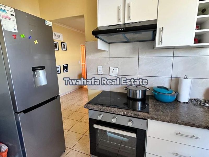 A functional kitchen featuring built-in cabinetry, a modern electric hob with extractor fan, tiled backsplash, and durable tiled flooring.